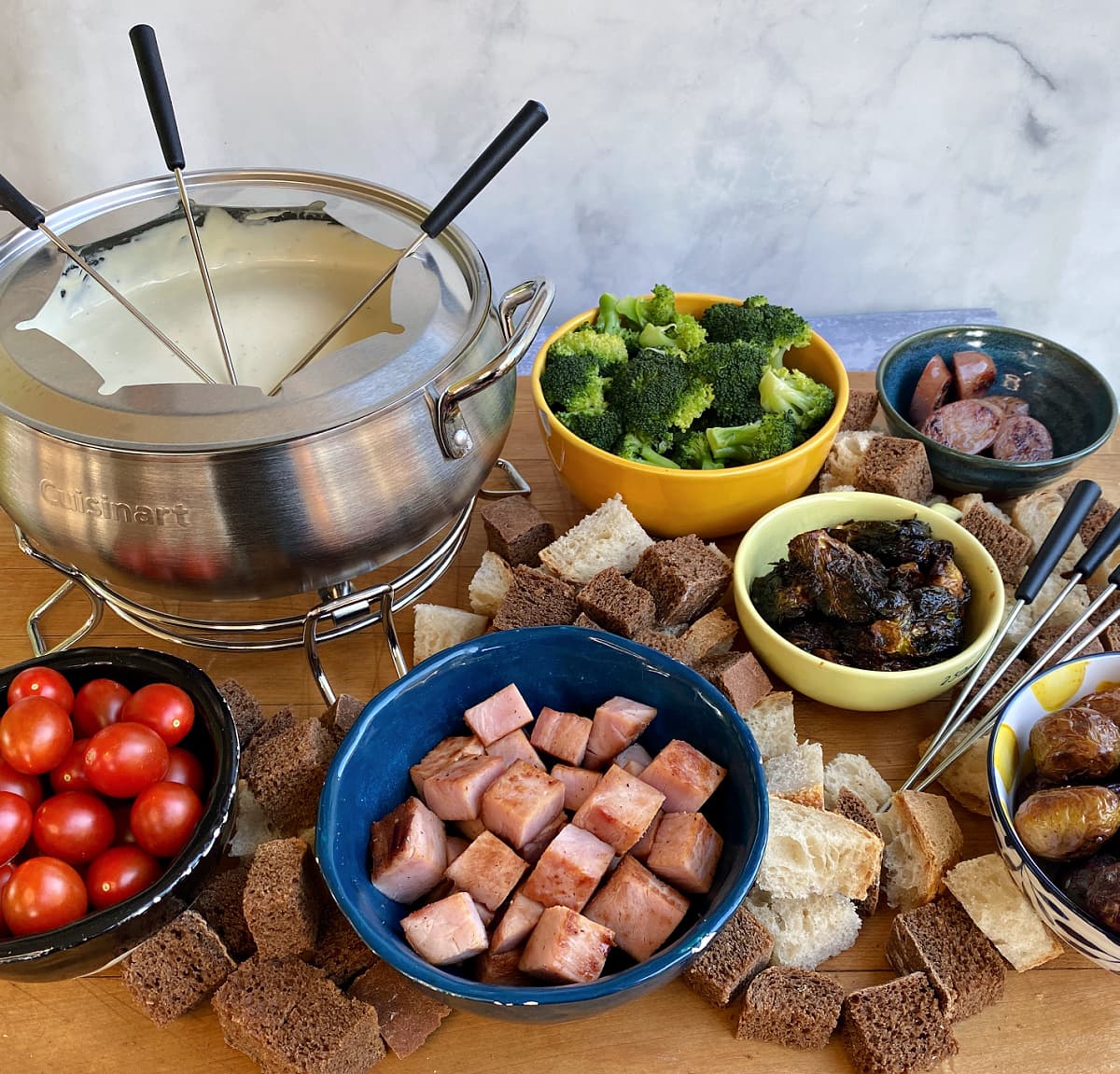 Party spread of fondue dippers, with a large fondue pot filled with melted cheese sauce. 