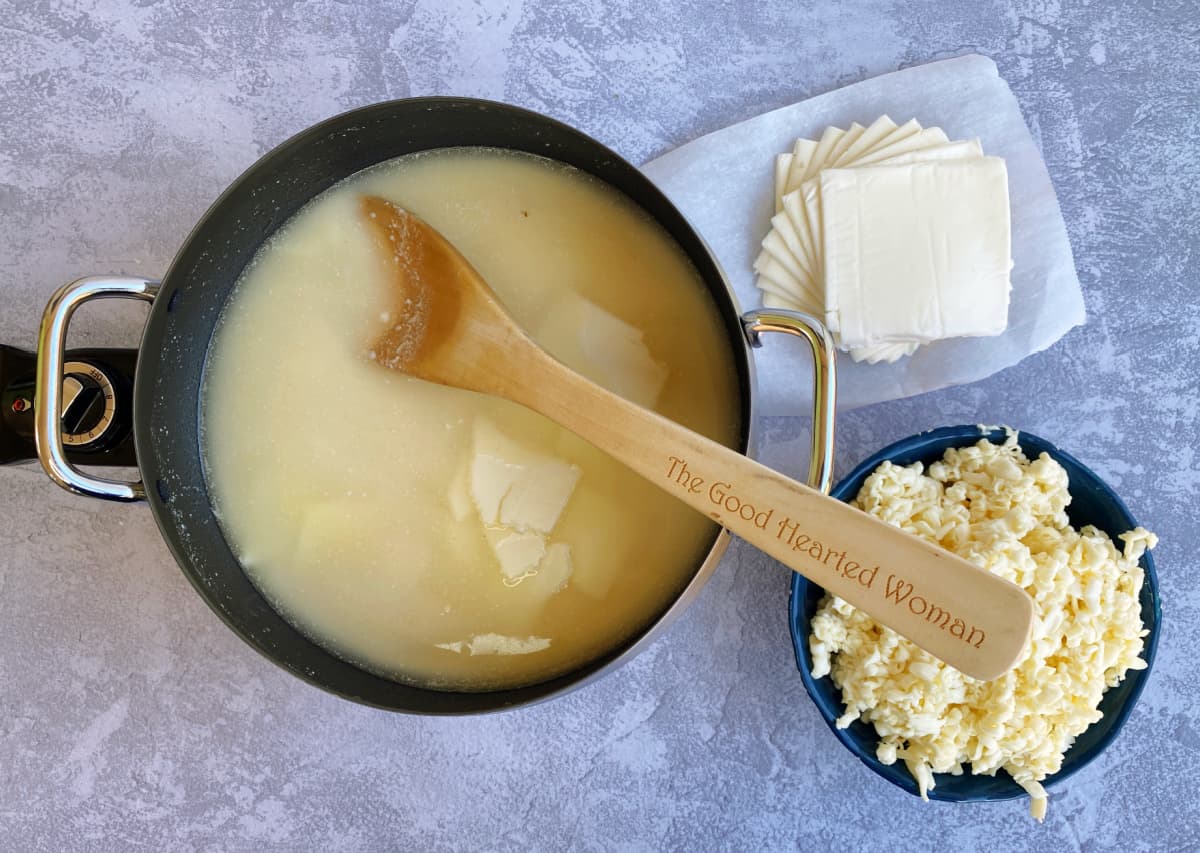 Fondue pot with liquid and some cheese added, more cheese on the side.