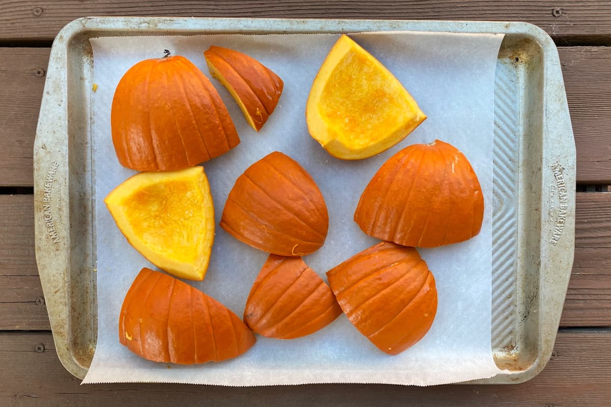 large pieces of cut pumpkin on a parchment lined baking sheet. 