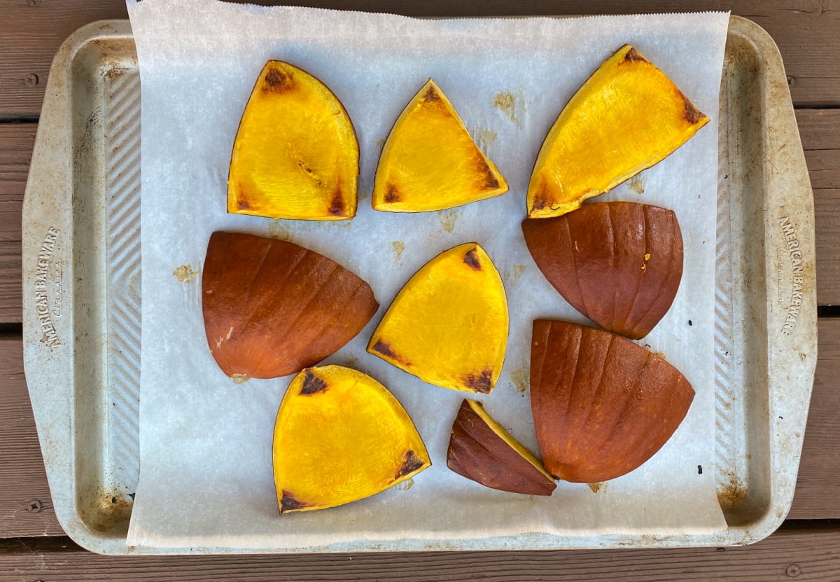 Cooked pumpkin pieces on a tray, some turned over to show browned edges on the underside. 