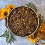 Overhead view of crockery bowl filled with baked stuffing, surrounded by fall decorations (sunflowers, fresh sage)