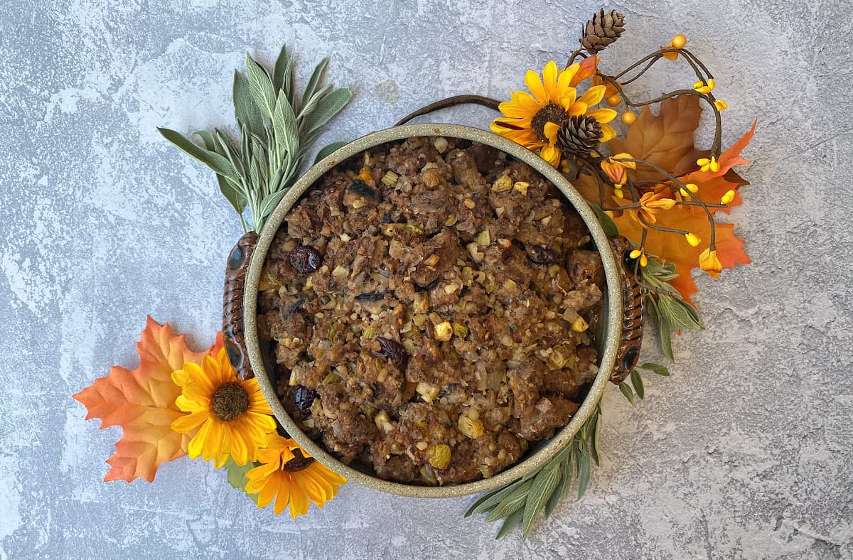 Crockery casserole dish filled with baked stuffing, surrounded by fall decorations (sunflowers, fresh sage). 
