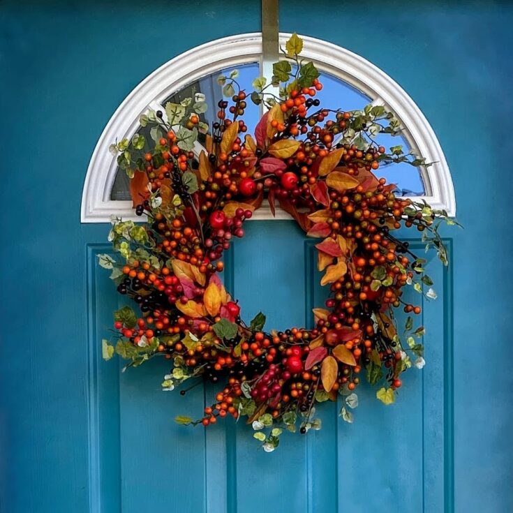 Fall-themed wreath hanging on a teal front door.