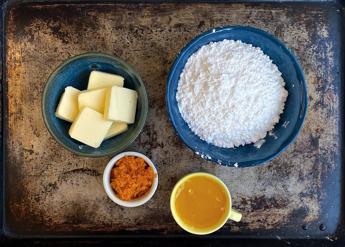 Orange icing ingredients on a tray: butter, orange juice & zest, and icing sugar.