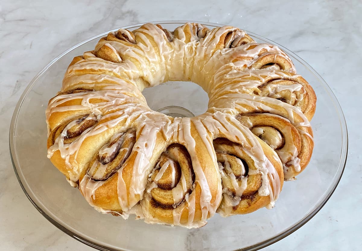 Cinnamon roll ring on baking tray, iced. Cinnamon roll ring on baking tray, iced. Cinnamon roll ring on a glass cake stand, iced and ready to serve.
