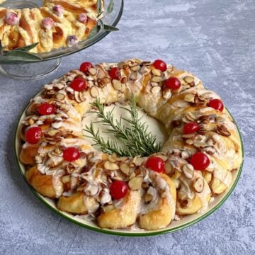 Cinnamon Danish ring garnished with caramelized almonds and cherries. Part of an orange ring in background.