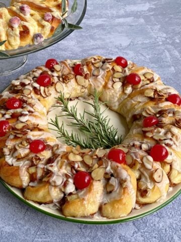 Cinnamon Danish ring garnished with caramelized almonds and cherries. Part of an orange ring in background.