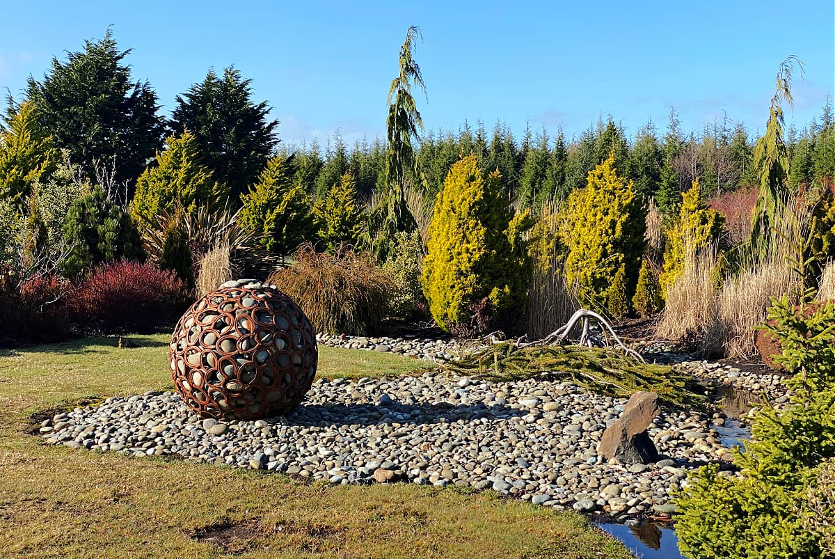 Large metal orb filled with smooth rocks, as displayed n garden.