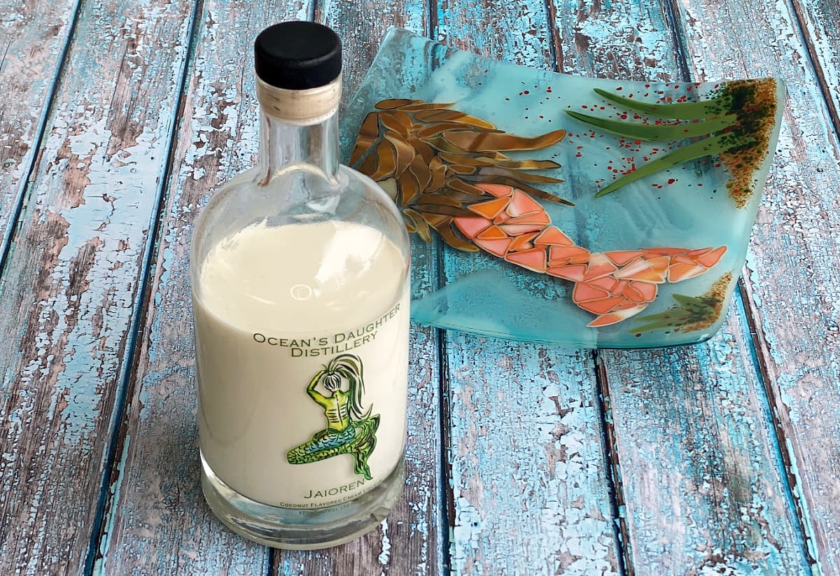 Bottle of coconut cream liqueur from Ocean's Daughter Distillery. Mermaid painted on the front label in shades of green. 