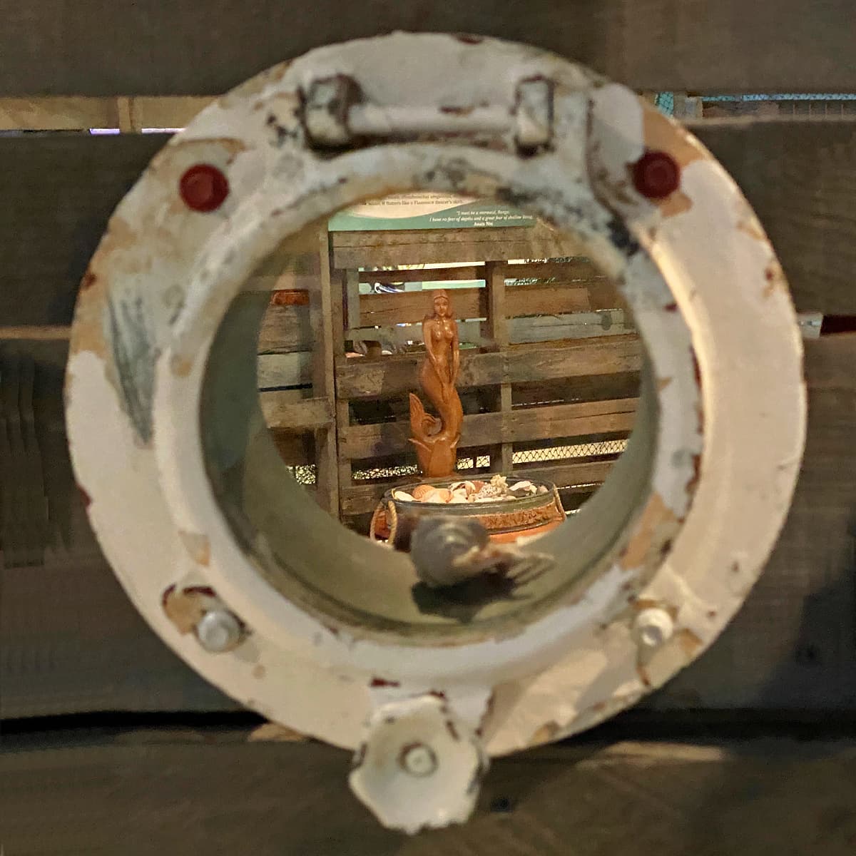 Porthole with a carved wooden mermaid in focused thru window. 