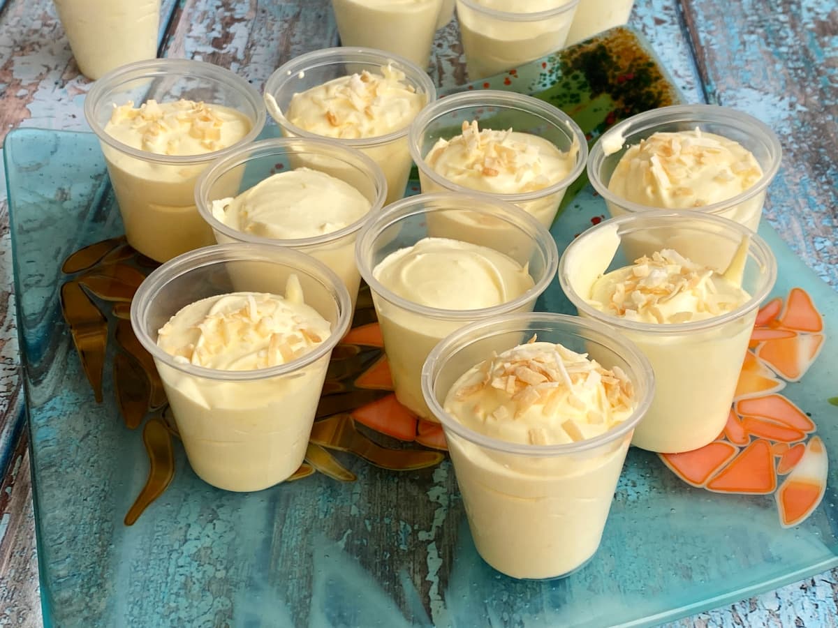 Small shot-size plastic cups filled with pudding mixture; some garnished with toasted coconut. 