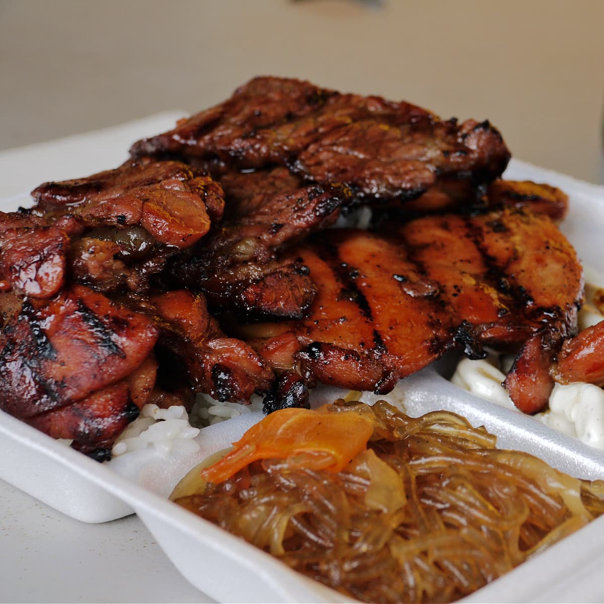 Hawaiian BBQ Chicken in a Styrofoam takeout box, with rice, macaroni salad, and glass noodles on the side.  