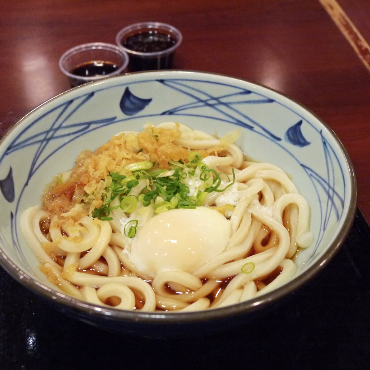 Bowl of udon noodles with a poached egg, crisp onions, and green onions. 