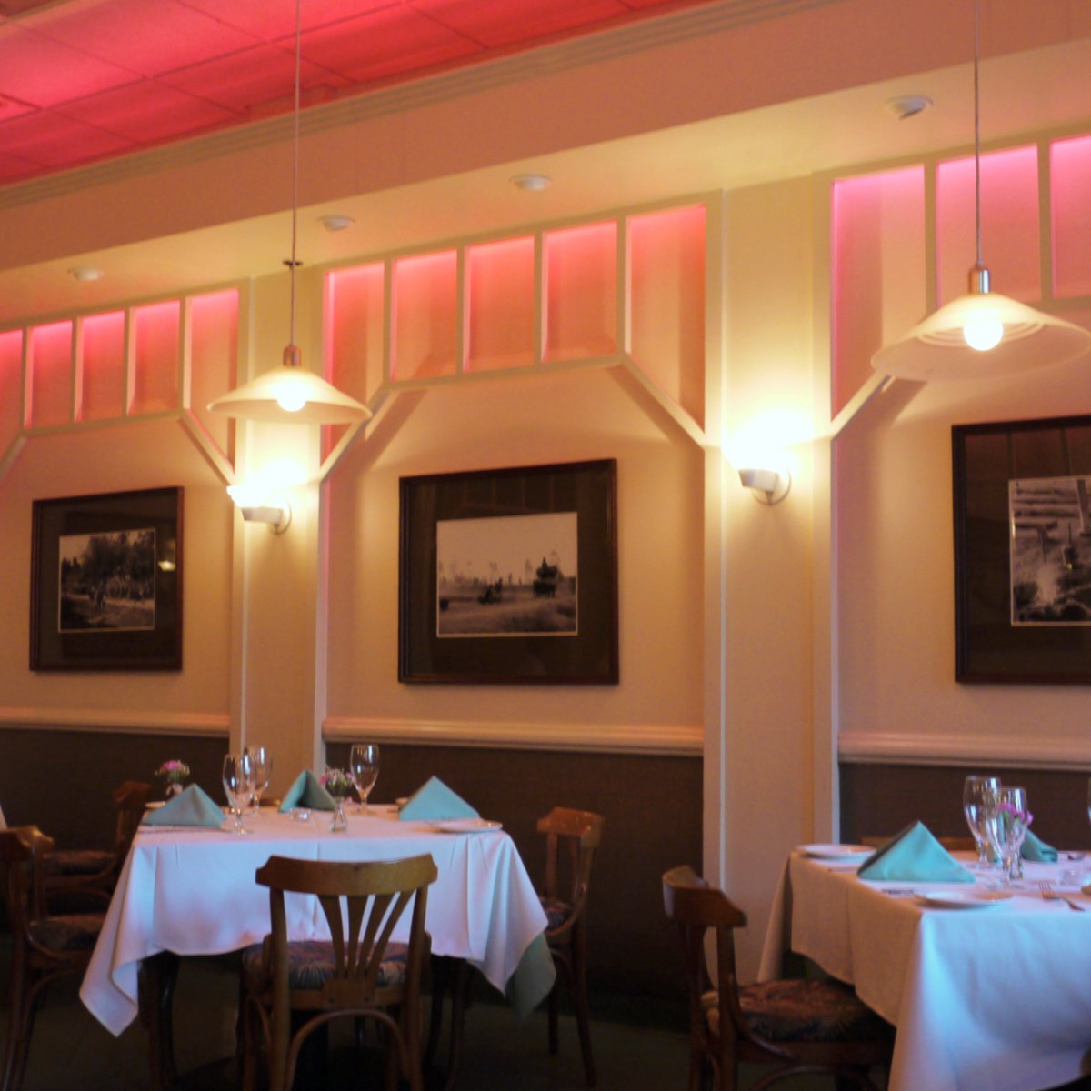 Interior of Duc's Bistro: soft pink lighting, dressed tables with folded, peaked napkins, simple wooden chairs. 