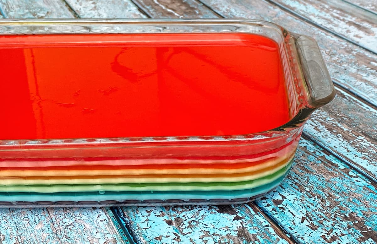 Side view of a glass 9x13 dish filled with rainbow jello, showing individual layers. 