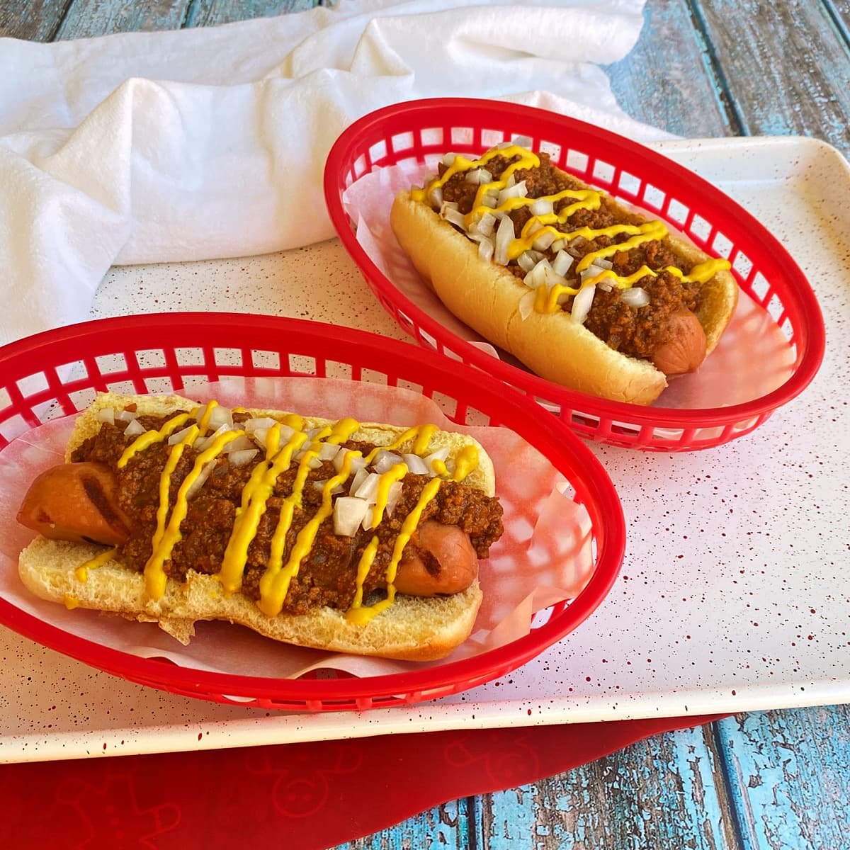 Two Coney Island hotdogs garnished with onions and yellow mustard, in red plastic fast food baskets. 