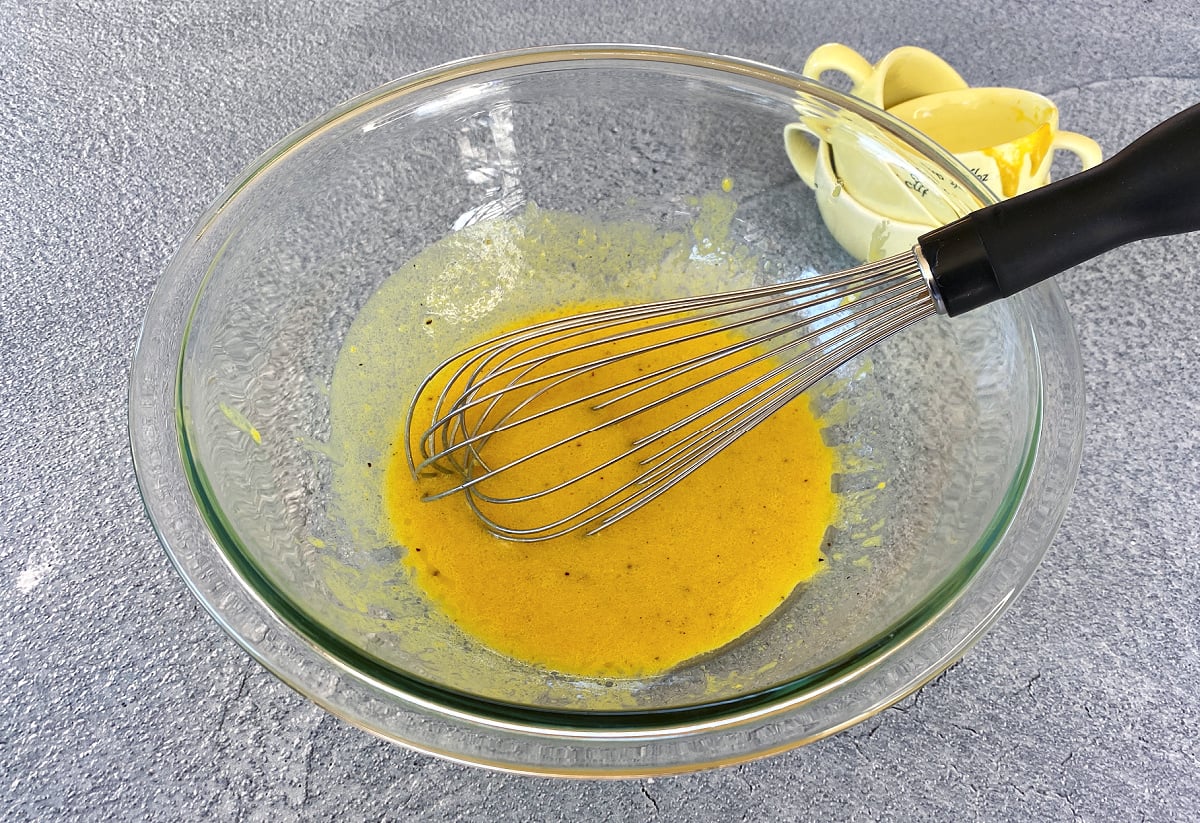 Glass mixing bowl with vinaigrette ingredients and wire whisk.