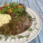 Plated Salisbury steak with gravy, plated with a green salad and mashed potatoes.