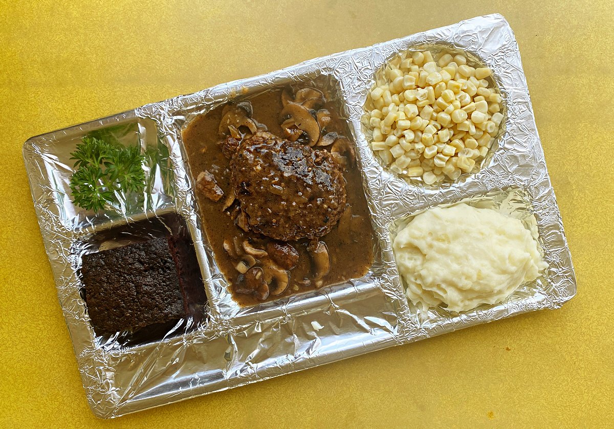 Divided foil tray with mashed potatoes, corn, chocolate cake, and one salisbury steak.