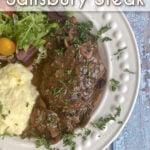 Plated Salisbury steak with gravy, plated with a green salad and mashed potatoes. Pin text reads: Homemade Salisbury steak / classic comfort food • one pot prep • budget-friendly