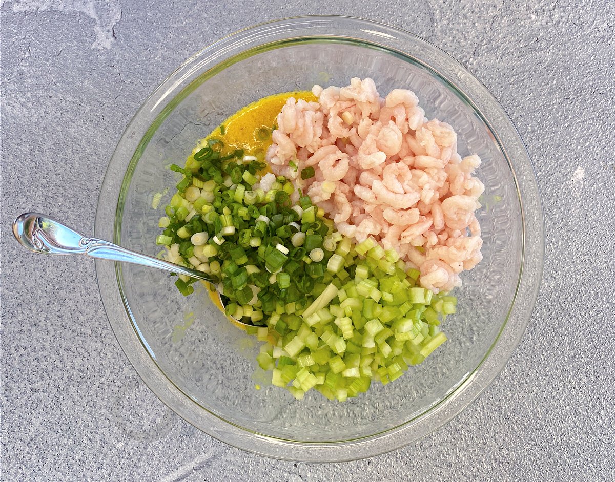 Green onions, celery, and shrimp added to mustard vinaigrette in a glass mixing bowl. 