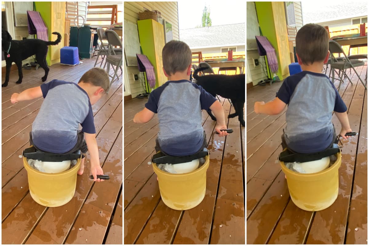 Toddler (viewed from the back) sitting on top of old ice cream churn, turning handle. 