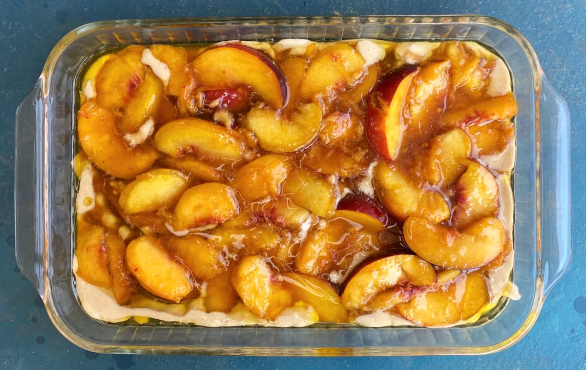 Fresh peach slices over batter in a glass baking dish.