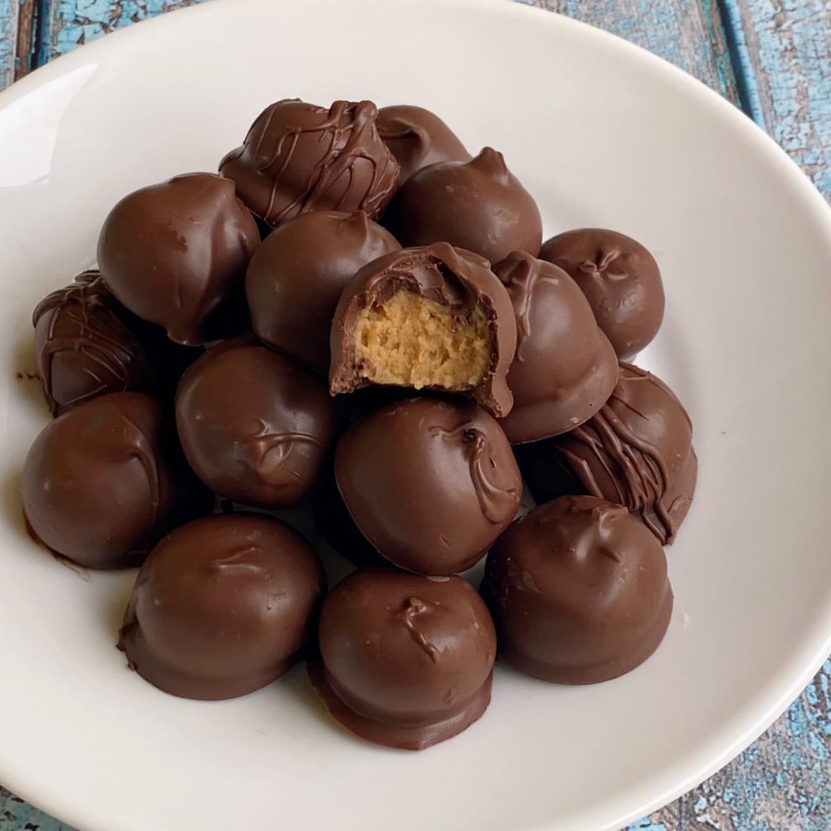 Many peanut butter balls stacked on a plate. One on top has a bite taken out to show center. 