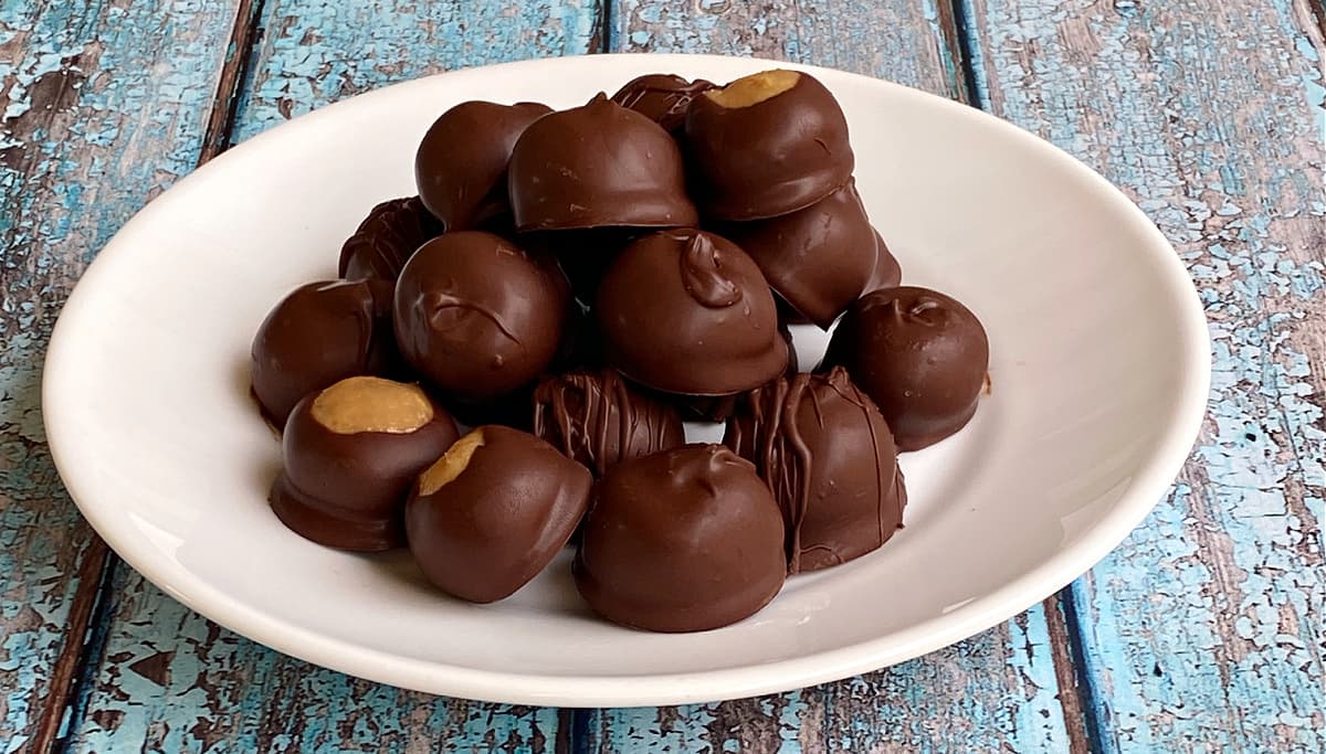 Peanut butter balls stacked on a plate. Three have been half-dipped, as with Buckeyes.