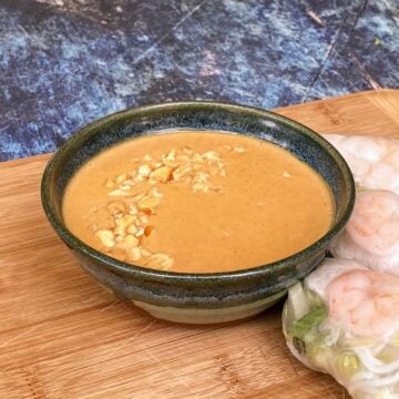 Small bowl of peanut sauce with chopped peanut sprinkled on top. More fresh rolls at the foot of the bowl.