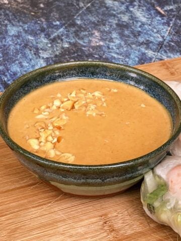 Small bowl of peanut sauce with chopped peanut sprinkled on top. More fresh rolls at the foot of the bowl.