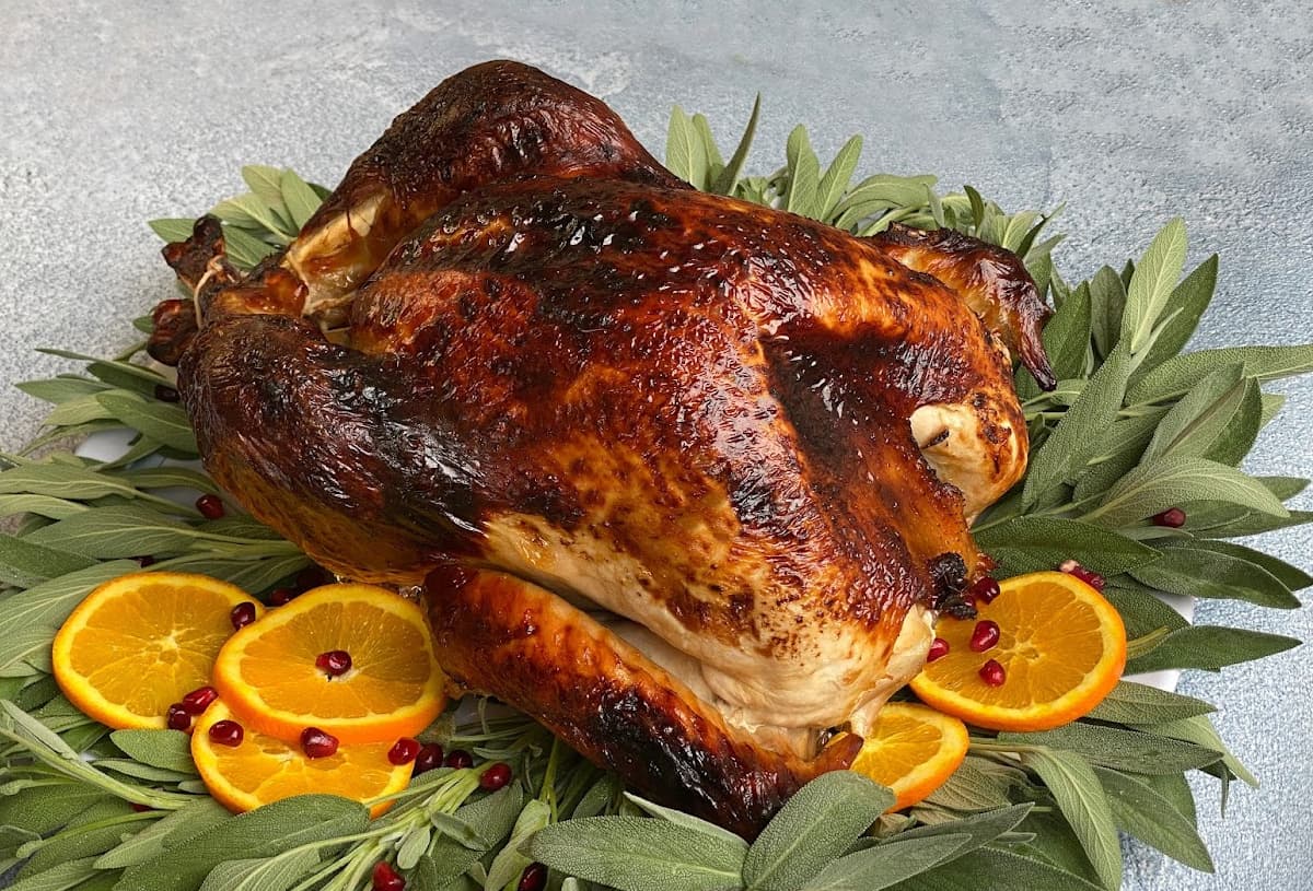 Oven roasted turkey on a platter, encircled with sage and garnished with orange slices and pomegranate arils.