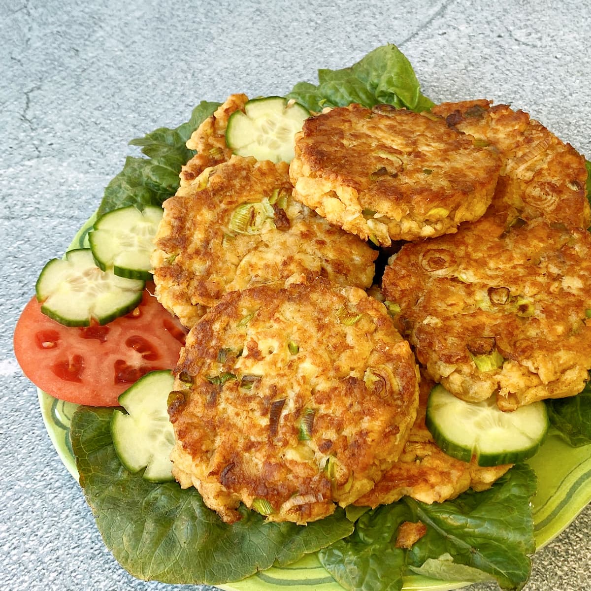 Plate stacked with pan-fried salmon patties, garnished with cucumber slices. 