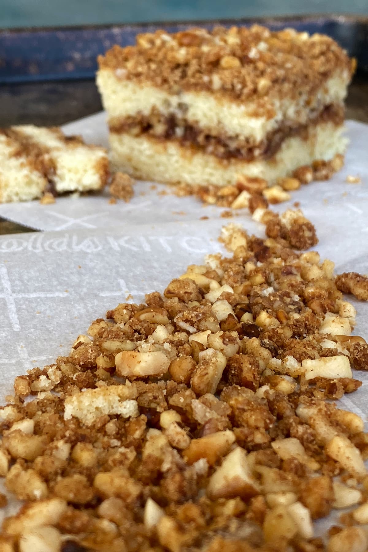 Nut streusel strewn in foreground leading to a cut square of streusel topped coffee cake in the background.