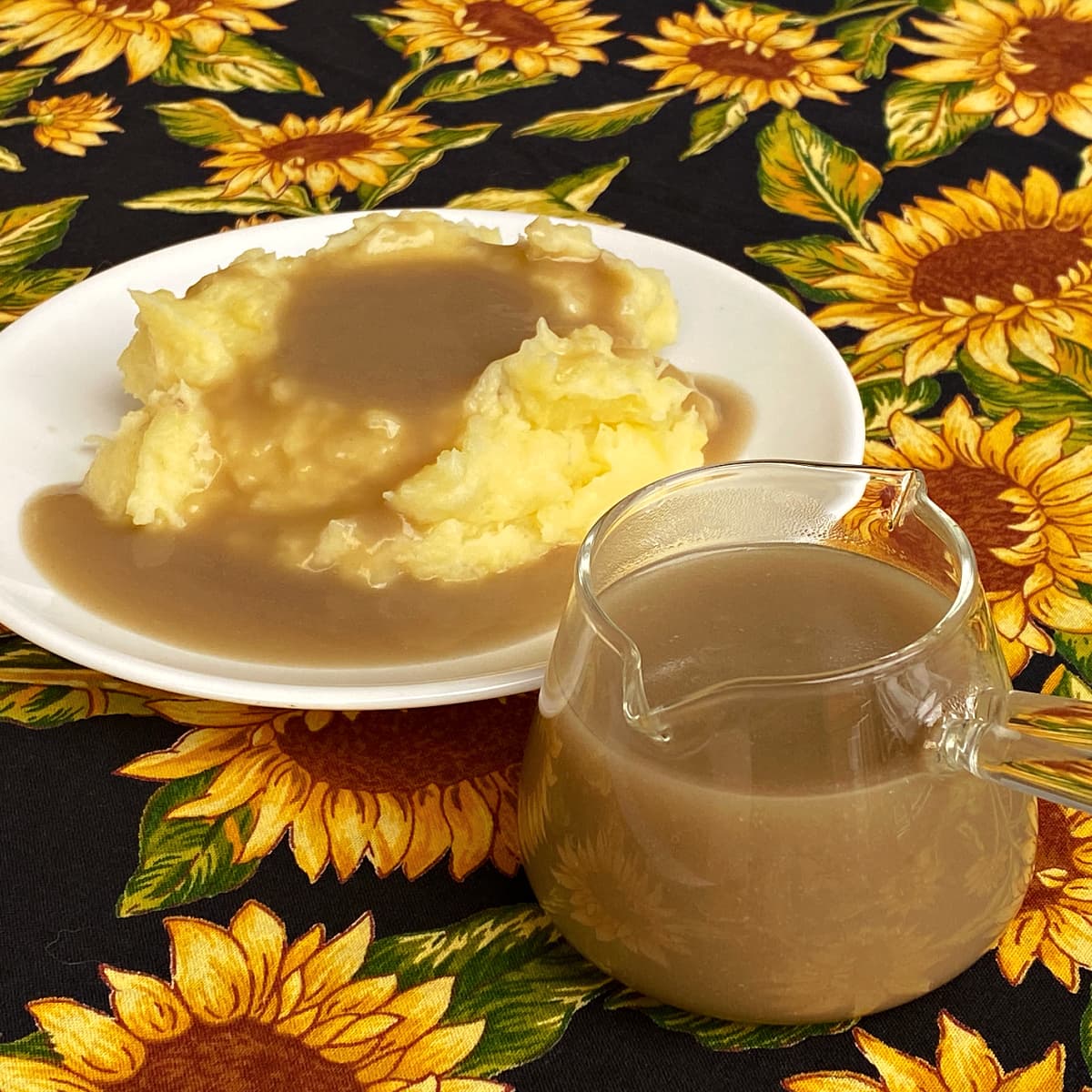 Turkey gravy in a glass sauce cup, and a small plate of mashed potatoes on a plate to the left.