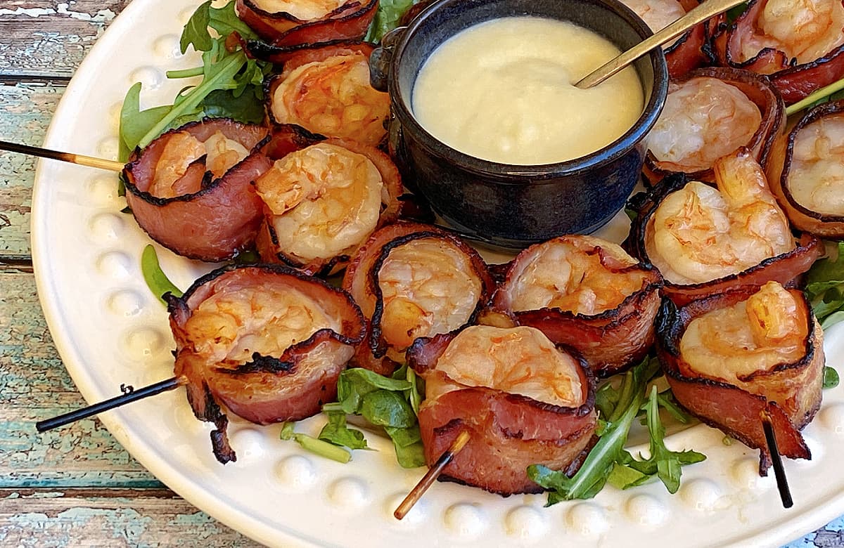 Plate of broiled, cooked bacon wrapped shrimps on a bed of arugula.