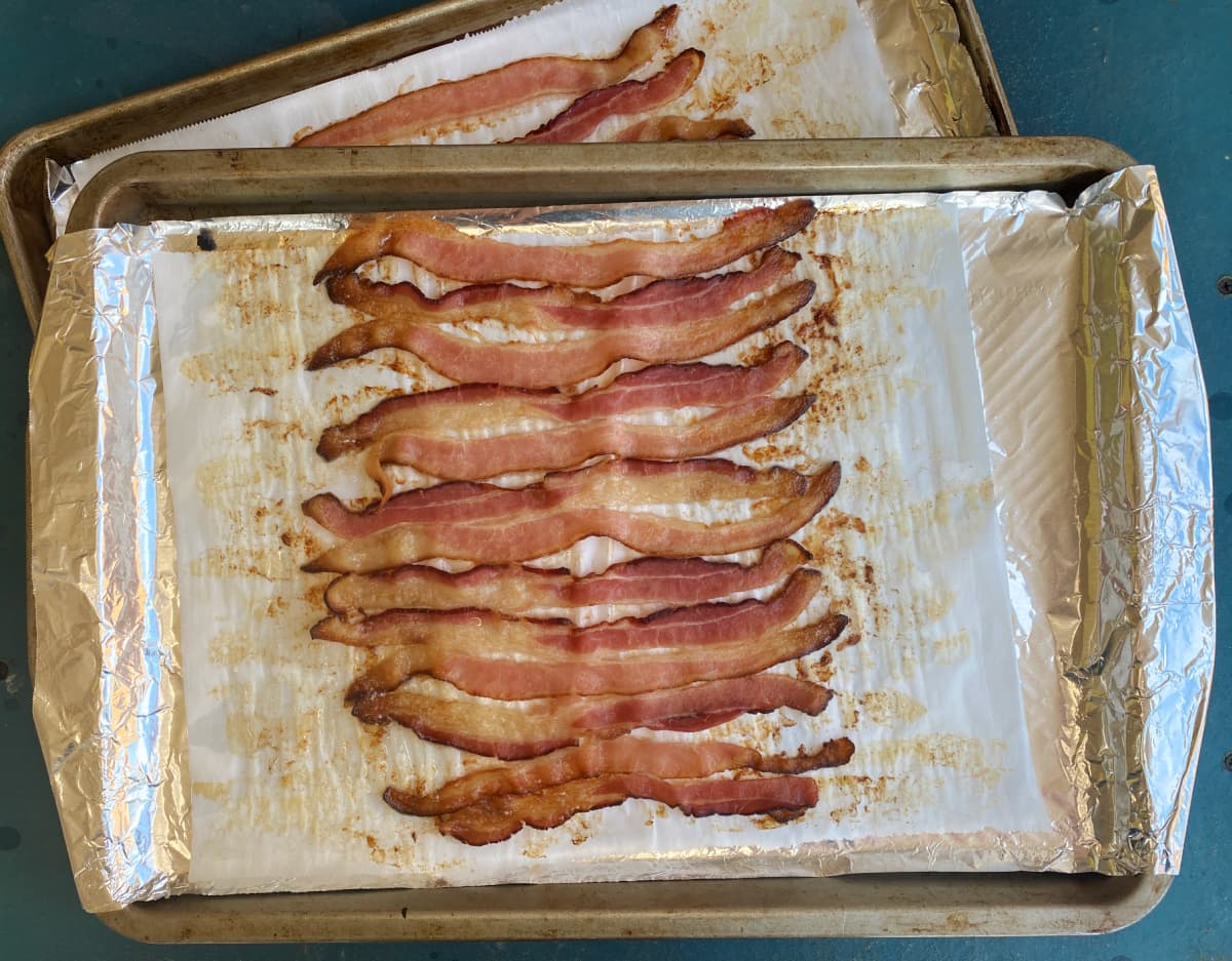 Bacon, sliced lengthwise, on baking sheet, cooked and cooling.
