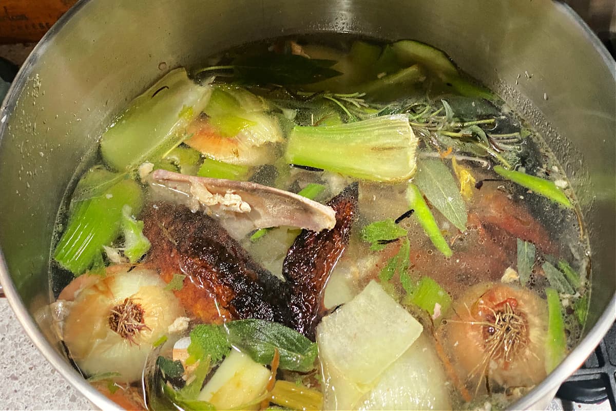 Overhead shot of a turkey carcass, vegetable scraps, and water in a large stockpot.