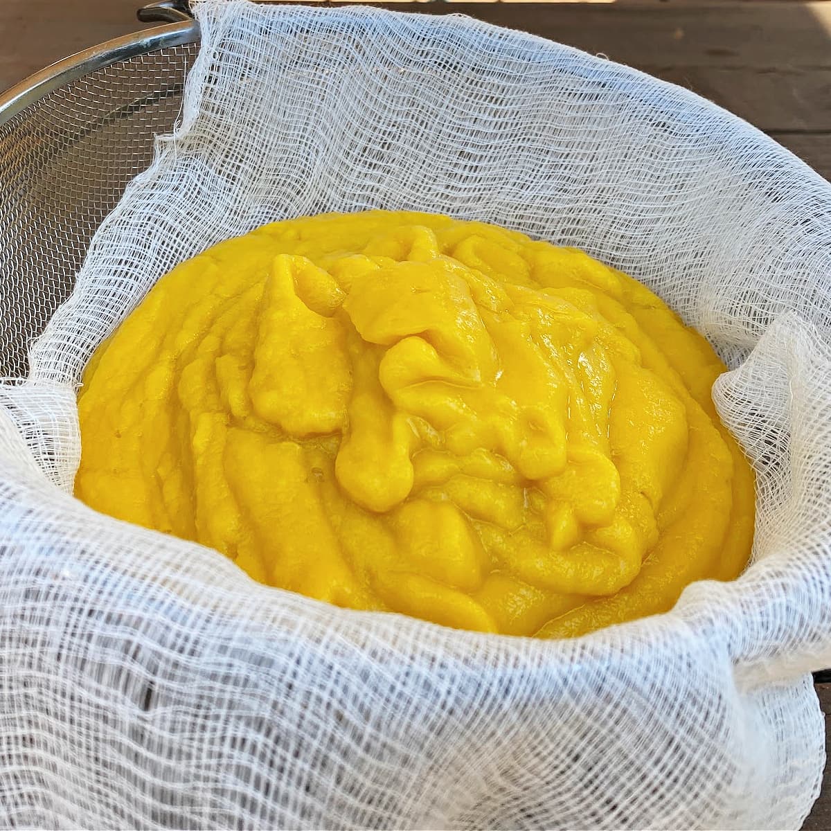 Pureed pumpkin draining in a cheesecloth-lined wire sieve. 
