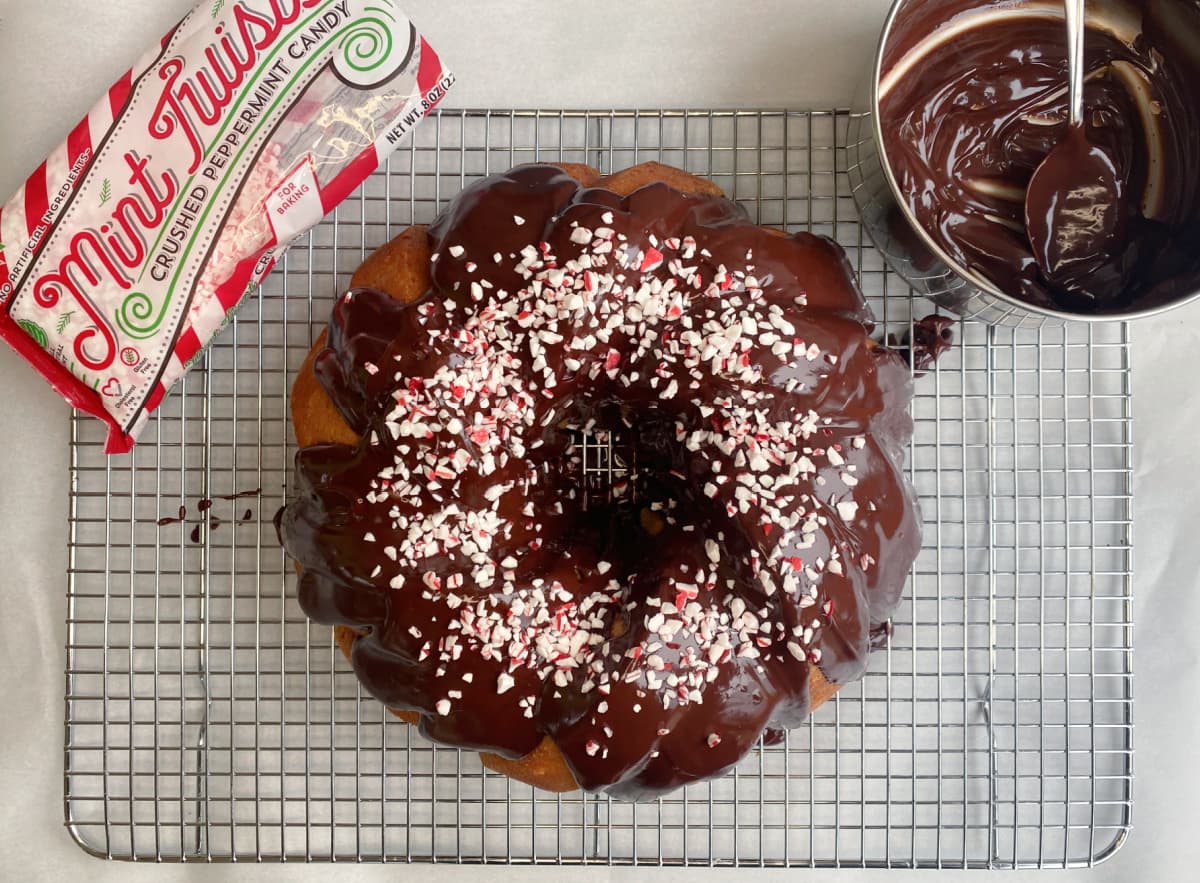 Overhead shot of Peppermint White Chocolate Bundt Cake with ganache and peppermint sprinkles added to top, with ganache pan and peppermint to the side.