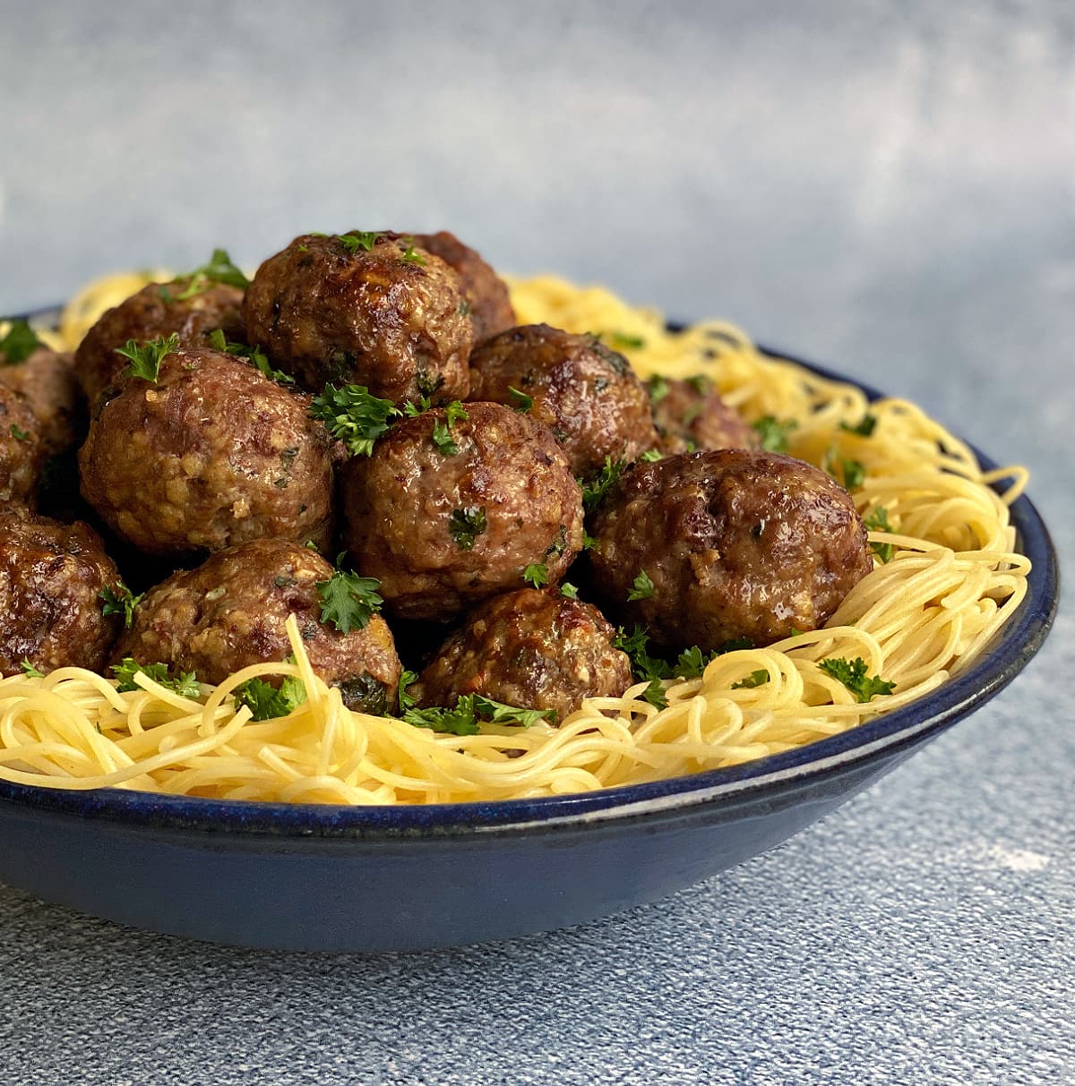 Bowl of cooked spaghetti noodles with a pile of baked ricotta meatballs in the center, garnished with chopped parsley.