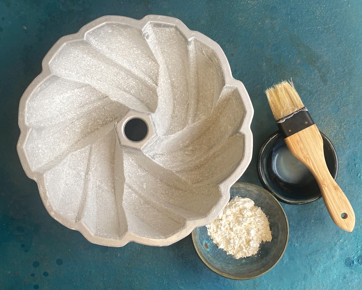 Prepared bundt pan with a small bowl of flour, pastry brush, and melted shortening on the side.