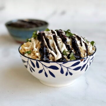 Rice bowl filled with brown rice, Oaxaca cheese, and topped with sour cream and Boss Sauce.