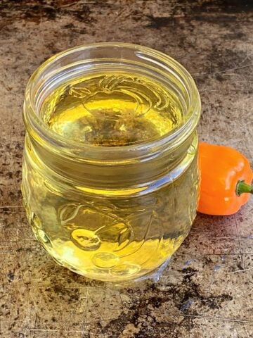 Small glass jar filled with habanero syrup, with one small habanero pepper sitting to the side.