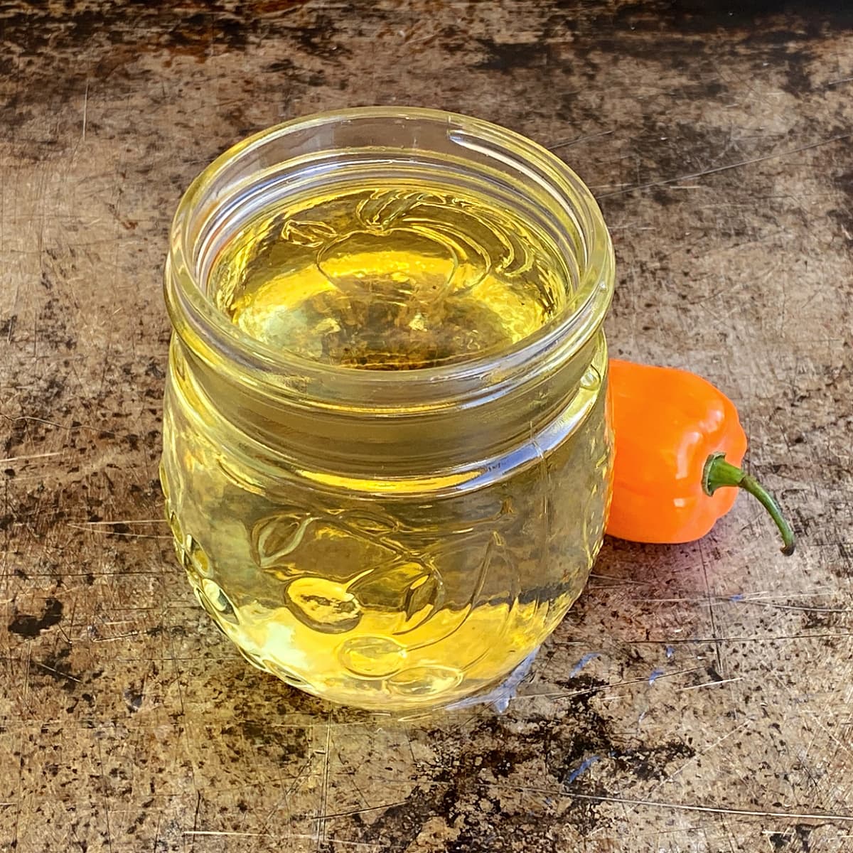 Small glass jar filled with habanero syrup, with one small habanero pepper sitting to the side. 