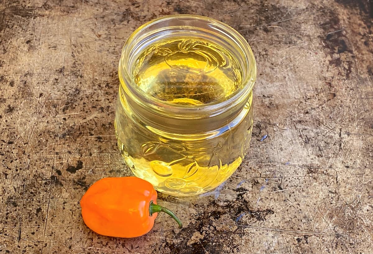 Small glass jar filled with habanero syrup, with one small habanero pepper resting near the front of the jar.