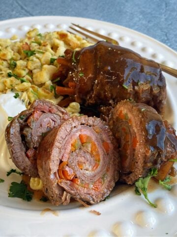 Two German Beef Rouladen rolls sliced on plate to show layered pinwheel, with sour cream and spätzle on the side.