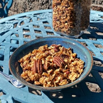 A bowl of pecan granola in a small bowl, setting on an outdoor bistro table.