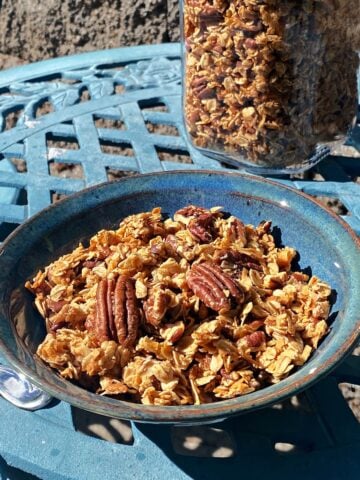 A bowl of pecan granola in a small bowl, setting on an outdoor bistro table.