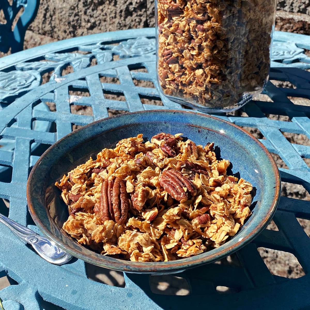 A bowl of pecan granola in a small bowl, setting on an outdoor bistro table. 